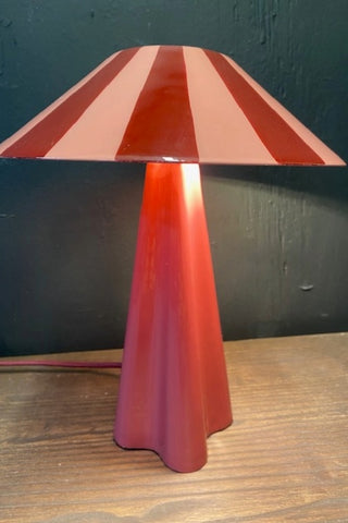 Image of the Deep Red Stripe Table Lamp on a dark surface against a black wall switched on.