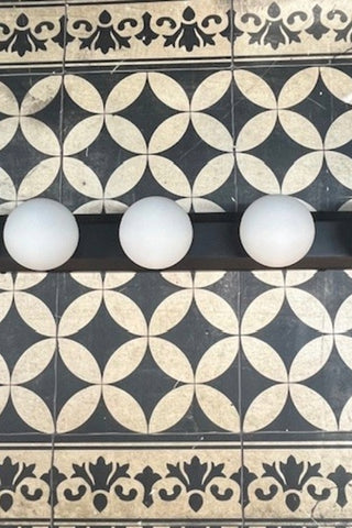 Close up of The Hollywood Vanity Wall Light in Black on a geometric floor.