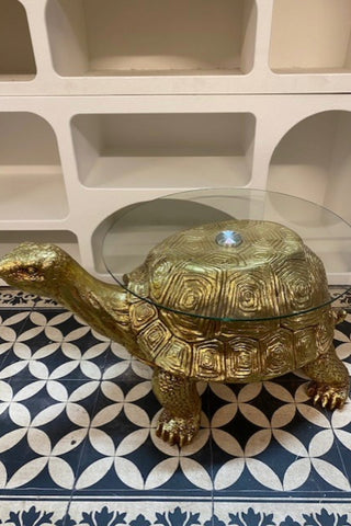 Side view of the Gold Tortoise Side Table on a patterned floor with white shelving behind it.