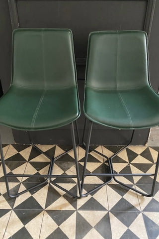 Set of two green bar stools with black legs on a geometric floor.