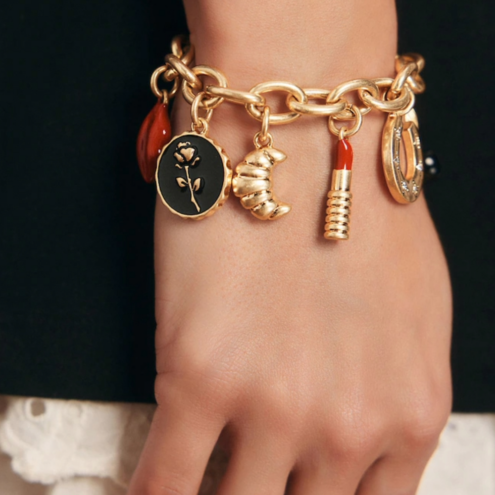 A beautiful charm bracelet with croissants, floral motifs, lipstick charms and a horseshoe charm on a womans hand.