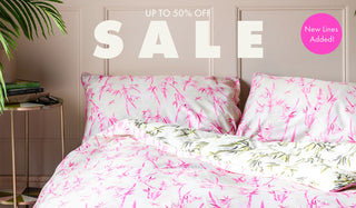 A bed with palm print bedding on, with the  words 'up to 50% off sale, new lines added!' above.