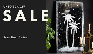 A mirror with white palm tree silhouettes on a dark background, shown leaning against a wall beside candles and a plant. Large sale text on the left reads 'UP TO 50% OFF SALE' and 'New Lines Added'.