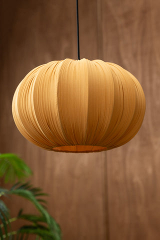 The Ochre Pleated Fabric Ceiling Light hanging in front of a dark background with a plant.