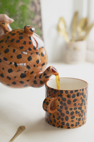 A leopard print teapot pouring tea into a leopard print mug.