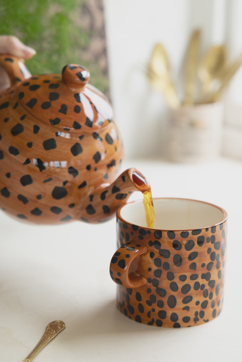 A leopard print teapot pouring tea into a leopard print mug.