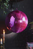 A video of the Hot Pink Disco Ball spinning, styled with some greenery, lit candles and books.