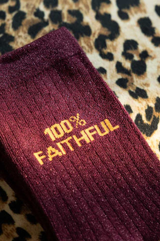 The 100% Faithful Burgundy Glitter Socks shown against a leopard print background. 