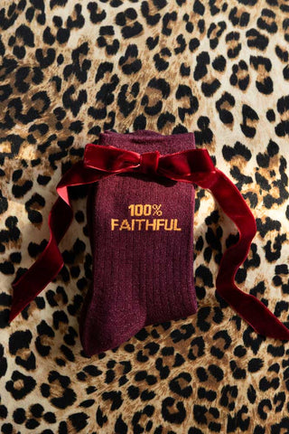 The 100% Faithful Burgundy Glitter Socks shown against a leopard print background with a red bow.