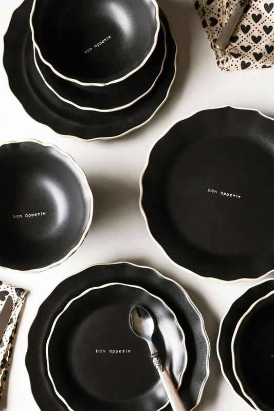 A birds eye view image of the 12 Piece Black & Off-White Edge Bon Apetit Dinner Set on a white table. 