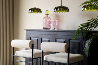 Rolled back white bar stools styled under a bar with green hanging ceiling lights.