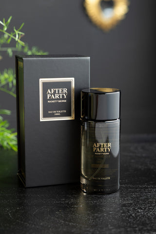 The After Party Eau de Toilette - 100ml and its box, displayed on a black surface with some greenery in the background.