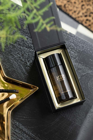The After Party Eau de Toilette - 100ml inside the box, seen from above on a dark surface with some accessories and greenery.