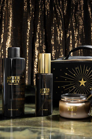 The contents of the After Party Makeup Bag Beauty Gift Set displayed in front of the bag, with a metallic background.