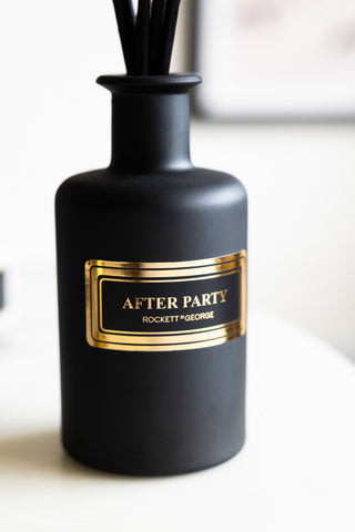 Close-up of a black reed diffuser with a gold label with the words 'after party' and the rockett st george logo on.