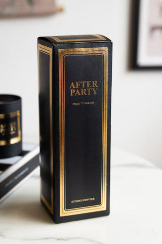 A black and gold diffuser box with the words after party on, styled on a whita table with a book and a candle.