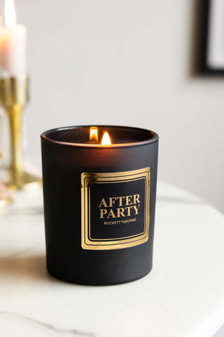 The After Party Freesia & Amber Scented Candle lit and displayed on a white surface.
