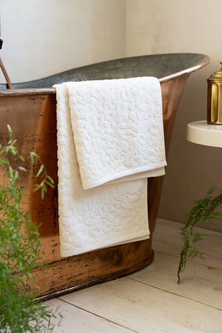 Leopard Jacquard Towel in Almond folded over a copper bath with plants in the background. 