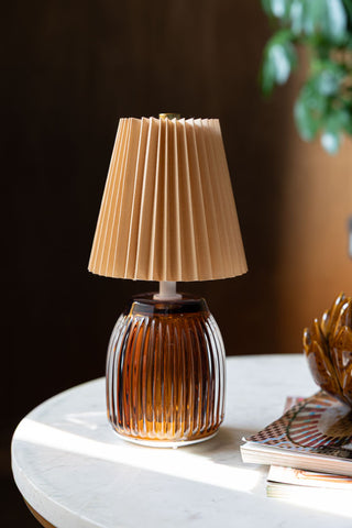 The Amber Pleated Rechargeable Table Lamp displayed on a white marble table with an ornament and some magazines.