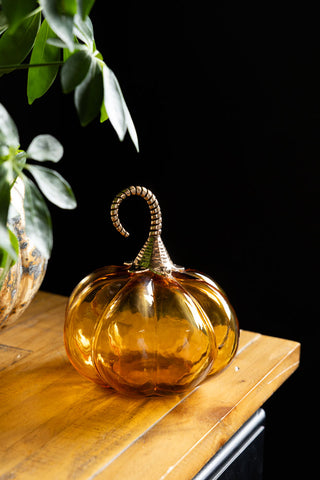 The Small Amber Glass Pumpkin shown on a wooden sideboard against dark walls. 
