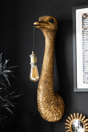 The Antique Bronze Ostrich Wall Light on a black wall, styled with a faux plant, framed artwork and mirror.