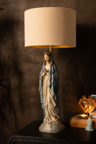 The Antique-Style Santa Maria Table Lamp styled on a sideboard with some other accessories in front of a dark wall.