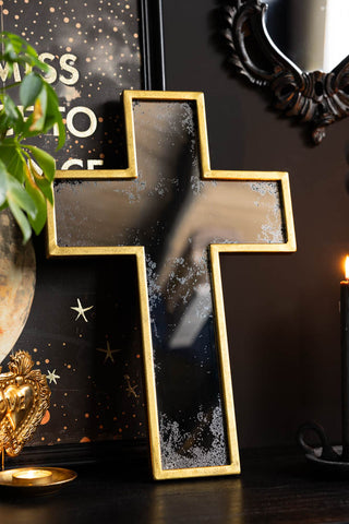 The Antique-style Gold Cross Wall Mirror shown against a black wall with quirky wall art. 