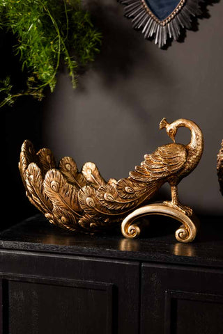 The Antique-Style Gold Peacock Decorative Display Bowl displayed on a black sideboard.