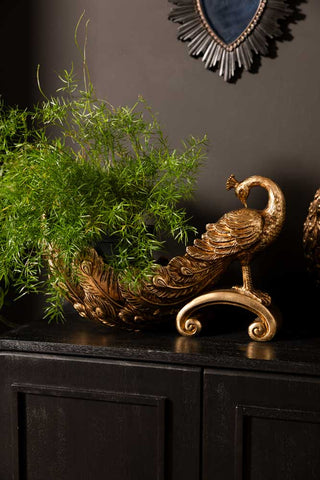 The Antique-Style Gold Peacock Decorative Display Bowl styled as a planter, displayed on a black sideboard.
