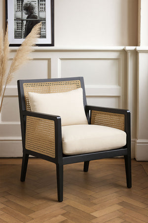 A styled image of the Artisan Wooden Framed Armchair Cream against a white wall and on a wooden floor. 