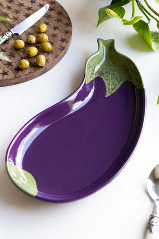 The Aubergine Serving Plate on a white table, displayed with a plant, star-patterned serving board, a knife and olives.