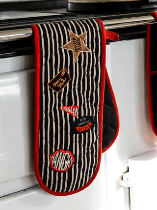 The Badge Patch Oven Gloves hanging on the front of a range cooker.