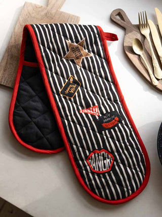 The Badge Patch Oven Gloves displayed on a wooden board on a kitchen work surface.