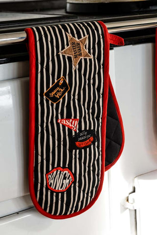 The Badge Patch Oven Gloves displayed on a rail in front of an oven.