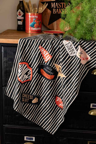 The Badge Patch Tea Towel hanging from a sideboard styled with various kitchen accessories.