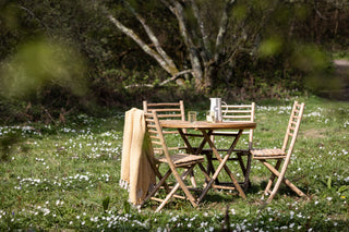 A pretty scene of Rockett St George bamboo table set in a field of wild flowers. There are 4 chairs and a table. 