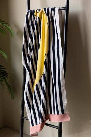 The Banana Beach Towel hanging on a black rail next to a plant.