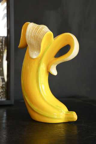 Lifestyle image of the Banana Vase displayed on a black sideboard with a mirror in the background. 