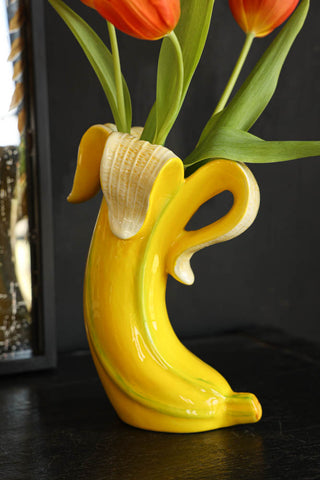 Lifestyle image of the Banana Vase styled on a black sideboard with tulips inside and a mirror in the background. 