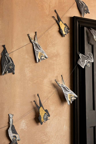 The Bats Sewn Paper Halloween Garland shown against a plaster wall and a black door. 