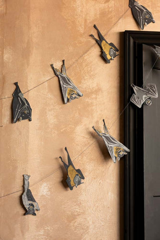 The Bats Sewn Paper Halloween Garland shown hanging against a plaster wall and black doorframe. 