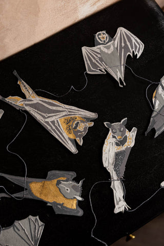 The bat designs of the Bats Sewn Paper Halloween Garland shown on a black sideboard. 