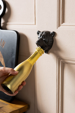 Image of the Bear Head Wall Mounted Bottle Opener opening a mini gold champagne bottle. 