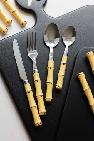 The Beautiful 16-Piece Bamboo Design Cutlery Set displayed on black serving boards on a white table.