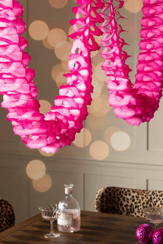 The Beautiful Handcrafted Classic Paper Garland in Hot Pink shown styled above a wooden dining table with leopard dining chairs. 