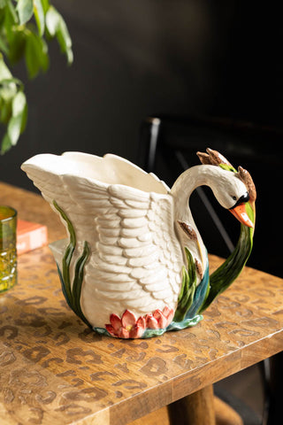 The Beautiful Painted Swan Jug displayed on a wooden surface with some accessories and a plant.