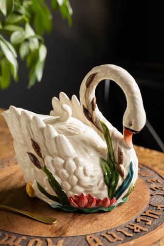 The Beautiful Painted Swan Teapot displayed on a wooden surface with a plant in the background.