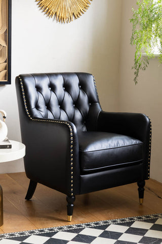 The Black Faux Leather Chesterfield Armchair styled in the corner of a room by a side table, with various accessories.