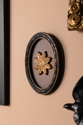 The Black Framed Golden Mystic Eye Wall Decor displayed on a wall with other wall art.