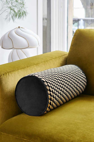 Lifestyle image of the Black Geo Bolster Cushion displayed on a yellow sofa with a lamp next to it.